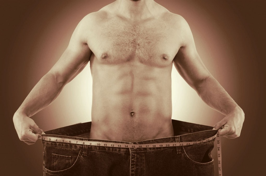 muscular man in oversized jeans holding them out to illustrate weight loss concept