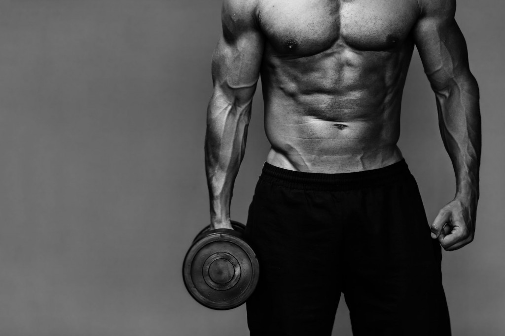 Close up of muscular bodybuilder guy doing exercises with weights over grey background - Black and white