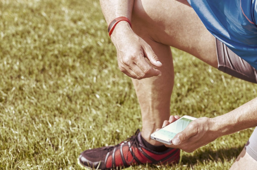 Sportive man kneels on a lawn and checks his fitness results on a smartphone