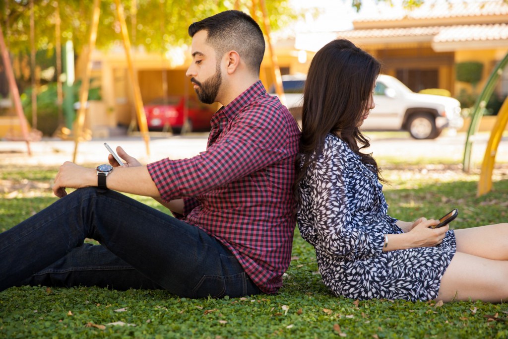 Profile view of a young couple ignoring each other by using their own smartphones