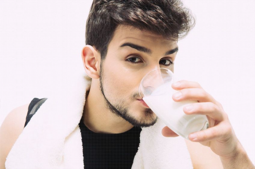 Sports man with towel drinking milk isolated on a white background.